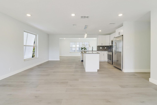 kitchen with plenty of natural light, appliances with stainless steel finishes, an island with sink, and white cabinets