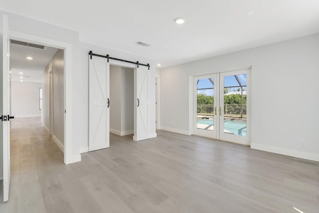 unfurnished bedroom featuring a barn door, access to exterior, light wood-type flooring, and french doors