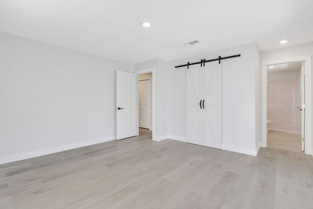 unfurnished bedroom with connected bathroom, a closet, light hardwood / wood-style flooring, and a barn door