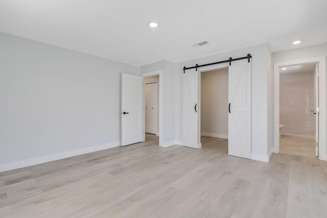 unfurnished bedroom featuring ensuite bath, a barn door, light hardwood / wood-style flooring, and a spacious closet