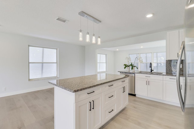 kitchen with appliances with stainless steel finishes, white cabinetry, light stone countertops, a kitchen island, and decorative light fixtures