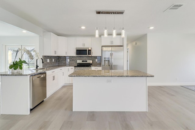 kitchen with sink, hanging light fixtures, stainless steel appliances, white cabinets, and a kitchen island