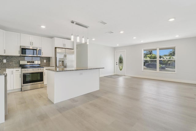 kitchen with dark stone countertops, hanging light fixtures, stainless steel appliances, white cabinets, and a kitchen island