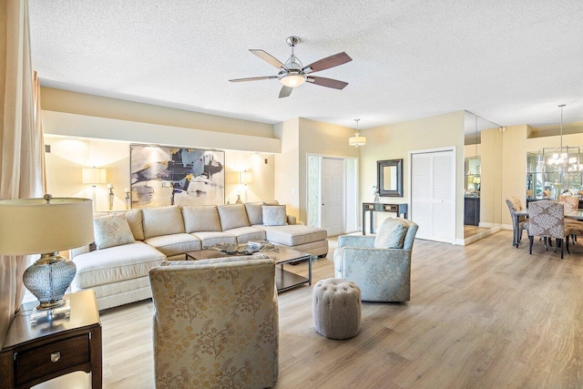 living area featuring light wood-type flooring, ceiling fan with notable chandelier, baseboards, and a textured ceiling