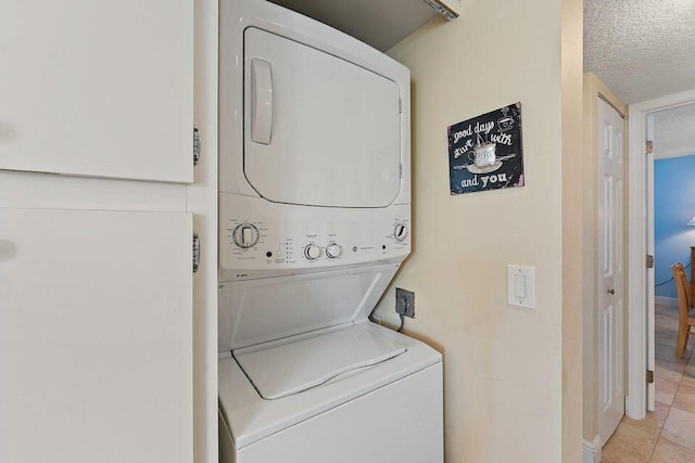 laundry area featuring laundry area, a textured ceiling, stacked washer / drying machine, and light tile patterned flooring