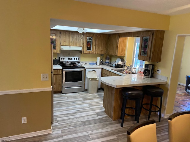 kitchen featuring a sink, a peninsula, stainless steel range with electric stovetop, under cabinet range hood, and a kitchen breakfast bar