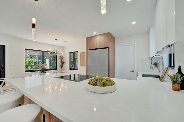 kitchen featuring sink, stainless steel refrigerator, a breakfast bar, hanging light fixtures, and white cabinets