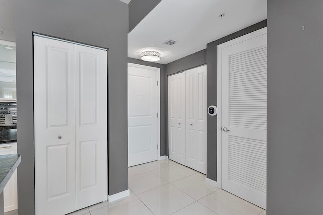 hall with visible vents, baseboards, and light tile patterned flooring