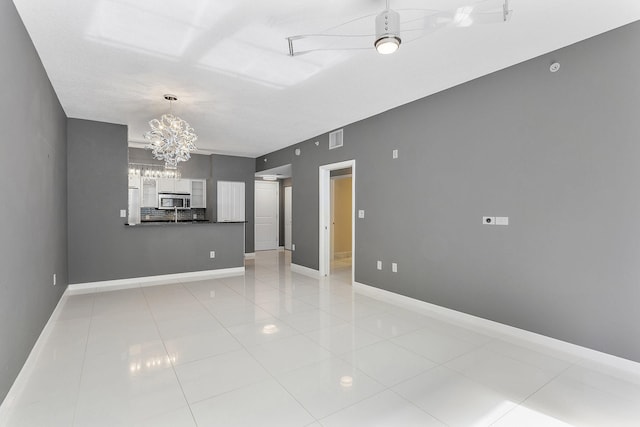 empty room featuring a chandelier, visible vents, baseboards, and light tile patterned floors