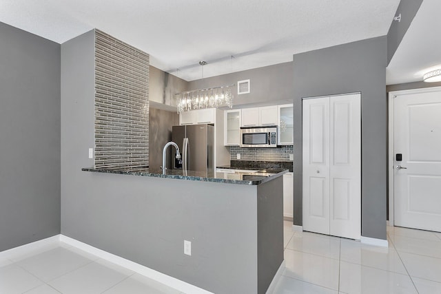 kitchen with appliances with stainless steel finishes, glass insert cabinets, dark stone countertops, a peninsula, and white cabinetry