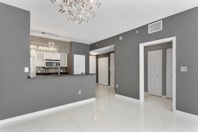 interior space with baseboards, light tile patterned flooring, visible vents, and an inviting chandelier