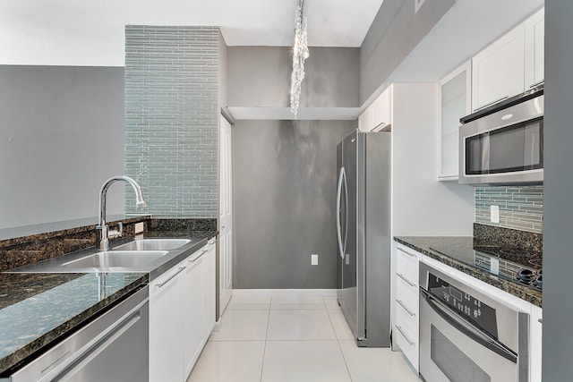 kitchen featuring light tile patterned floors, stainless steel appliances, decorative backsplash, white cabinets, and dark stone counters