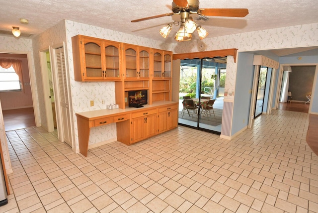 kitchen with a textured ceiling, light countertops, glass insert cabinets, and wallpapered walls