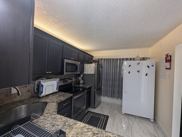 kitchen featuring sink, backsplash, stainless steel appliances, a textured ceiling, and dark stone counters