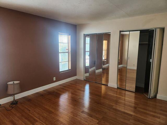 unfurnished bedroom with multiple closets and dark hardwood / wood-style floors