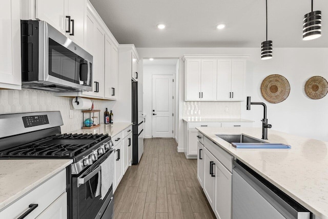 kitchen with hanging light fixtures, white cabinetry, appliances with stainless steel finishes, and sink