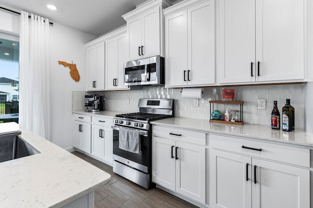 kitchen with stainless steel appliances, tasteful backsplash, light stone countertops, and white cabinets