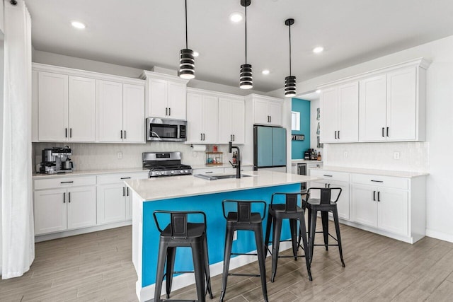 kitchen featuring appliances with stainless steel finishes, white cabinetry, sink, hanging light fixtures, and a kitchen island with sink