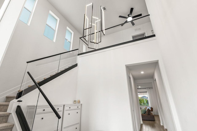 stairs with wood-type flooring, ceiling fan, and a high ceiling