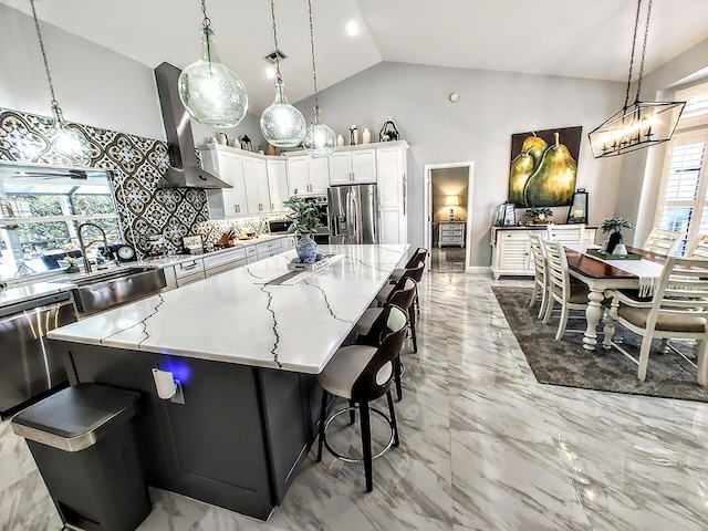 kitchen featuring decorative light fixtures, wall chimney range hood, a spacious island, stainless steel appliances, and white cabinets