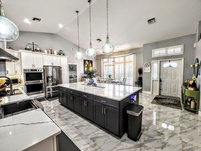 kitchen featuring appliances with stainless steel finishes, pendant lighting, vaulted ceiling, a center island, and white cabinetry