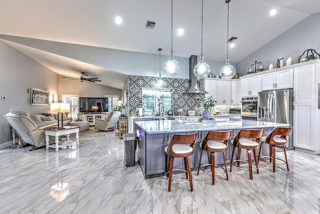 kitchen with decorative light fixtures, appliances with stainless steel finishes, white cabinets, a kitchen bar, and wall chimney exhaust hood