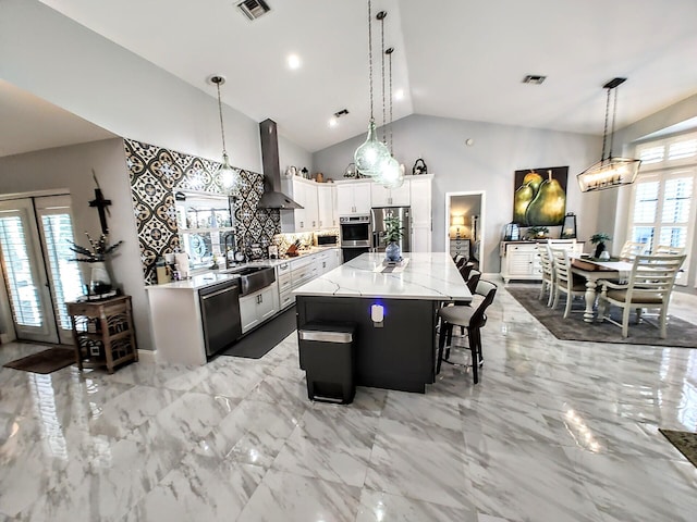 kitchen with appliances with stainless steel finishes, pendant lighting, a kitchen island, wall chimney exhaust hood, and white cabinets