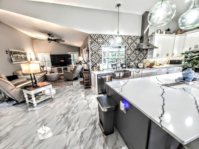 kitchen with lofted ceiling, sink, wall chimney exhaust hood, white cabinets, and hanging light fixtures