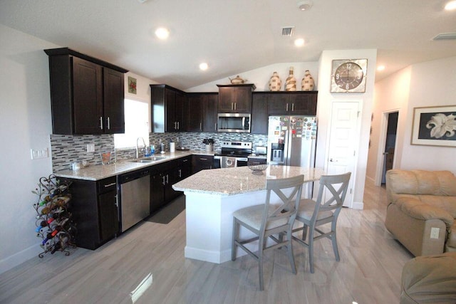 kitchen with vaulted ceiling, appliances with stainless steel finishes, a breakfast bar, sink, and a center island