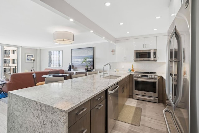 kitchen with stainless steel appliances, light stone countertops, sink, white cabinets, and decorative backsplash