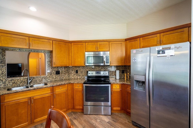 kitchen featuring a sink, backsplash, dark wood finished floors, appliances with stainless steel finishes, and brown cabinetry