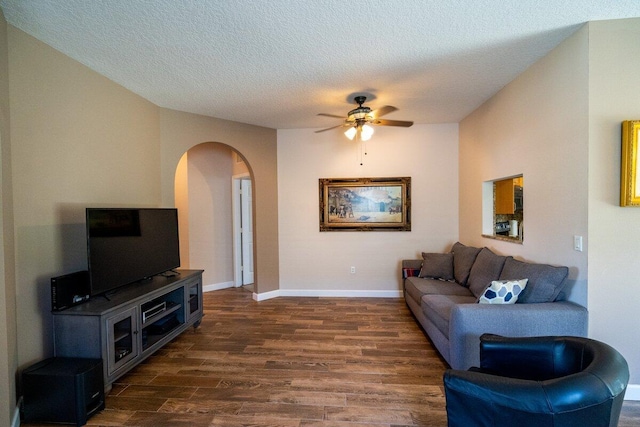 living room with a textured ceiling, dark wood-style floors, arched walkways, baseboards, and ceiling fan
