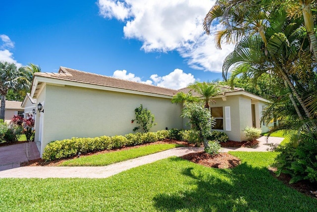 view of front of home with stucco siding, an attached garage, a tile roof, and a front lawn