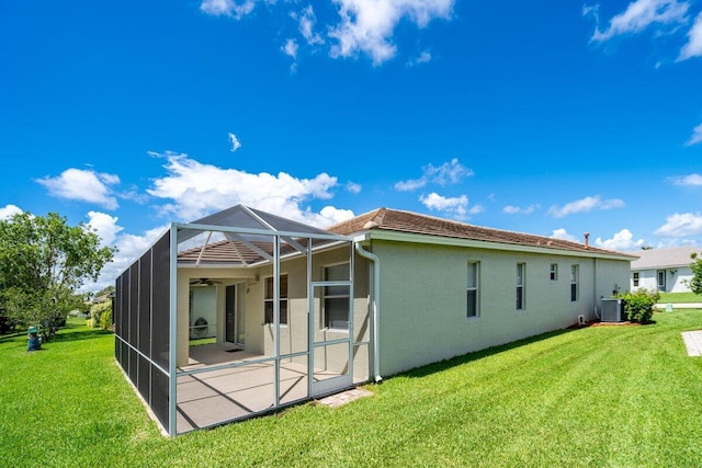 back of house with a lanai, central air condition unit, a yard, and stucco siding