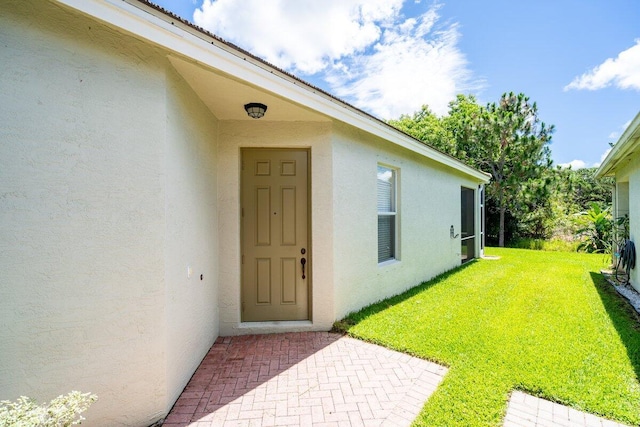 entrance to property featuring stucco siding and a lawn