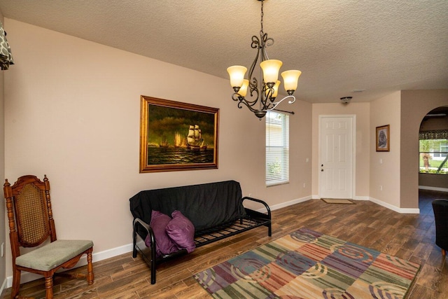 sitting room featuring a textured ceiling, dark wood finished floors, arched walkways, an inviting chandelier, and baseboards