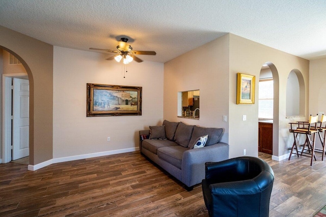 living room with arched walkways, dark wood-style floors, a textured ceiling, and baseboards