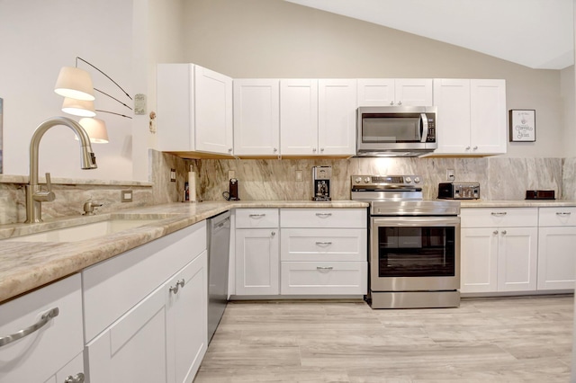 kitchen with decorative backsplash, lofted ceiling, appliances with stainless steel finishes, white cabinetry, and a sink