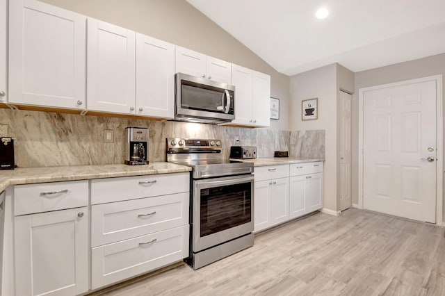 kitchen with lofted ceiling, tasteful backsplash, appliances with stainless steel finishes, and white cabinets