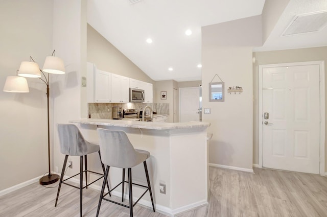 kitchen featuring stainless steel appliances, a peninsula, white cabinetry, backsplash, and a kitchen bar