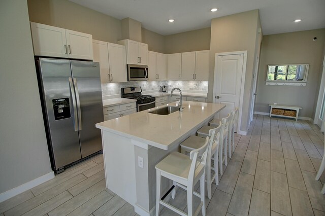 kitchen with stainless steel appliances, a sink, white cabinets, decorative backsplash, and wood tiled floor