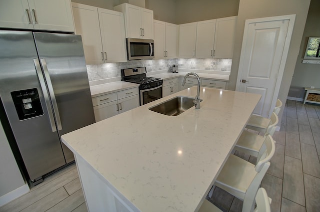 kitchen featuring stainless steel appliances, backsplash, a sink, and a kitchen island with sink