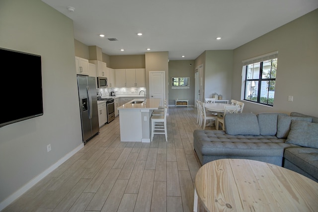 kitchen with stainless steel appliances, a sink, white cabinetry, a kitchen breakfast bar, and open floor plan