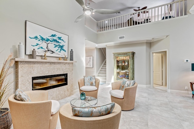 living room with a high end fireplace, ceiling fan, and a high ceiling