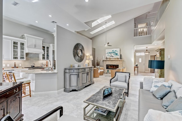 living room with sink, ceiling fan, a skylight, high vaulted ceiling, and a high end fireplace