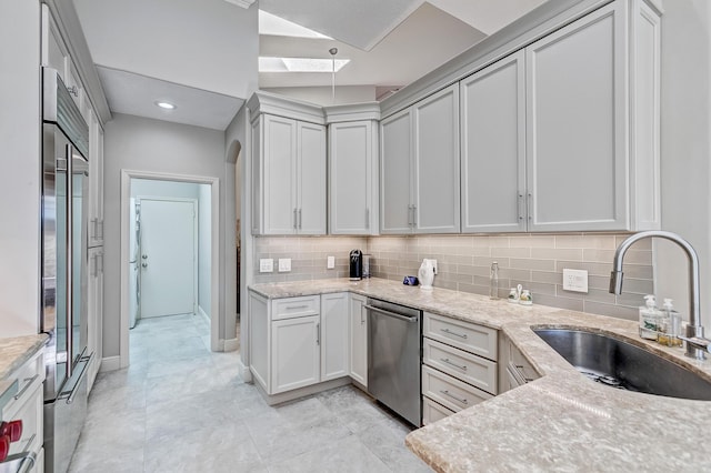 kitchen with appliances with stainless steel finishes, sink, light stone counters, and decorative backsplash