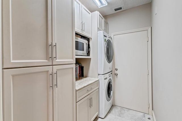 clothes washing area featuring cabinets, stacked washer / dryer, and a textured ceiling