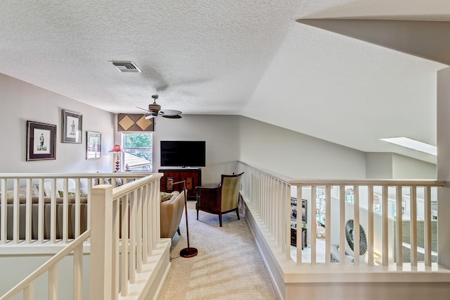 hallway with lofted ceiling with skylight, light colored carpet, and a textured ceiling