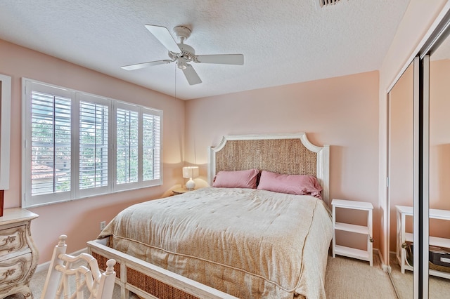 bedroom with ceiling fan, light colored carpet, a closet, and a textured ceiling