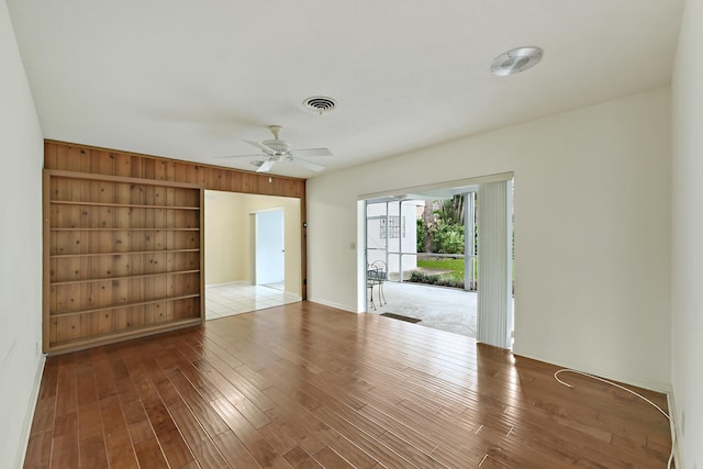 unfurnished room with ceiling fan, visible vents, built in features, and wood finished floors